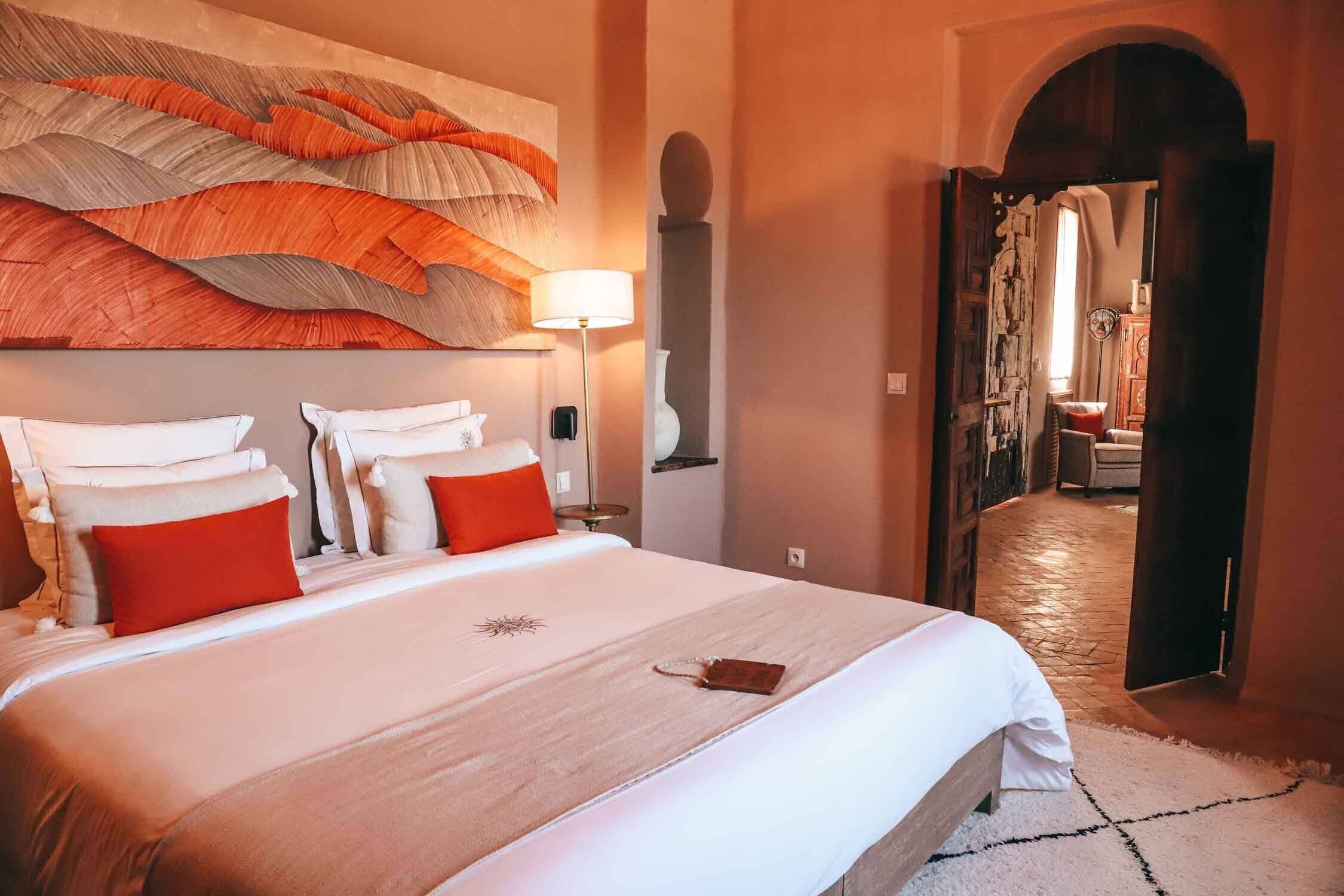 Una cama grande con ropa de cama blanca y roja, una obra de arte en la pared y una lámpara.
