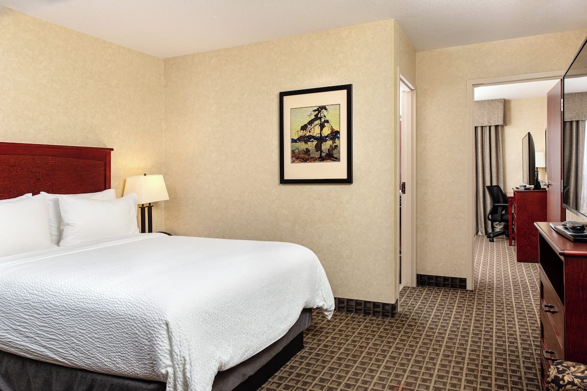 A hotel room with a large bed, a desk with a chair, a mirror, and a framed picture on the wall.