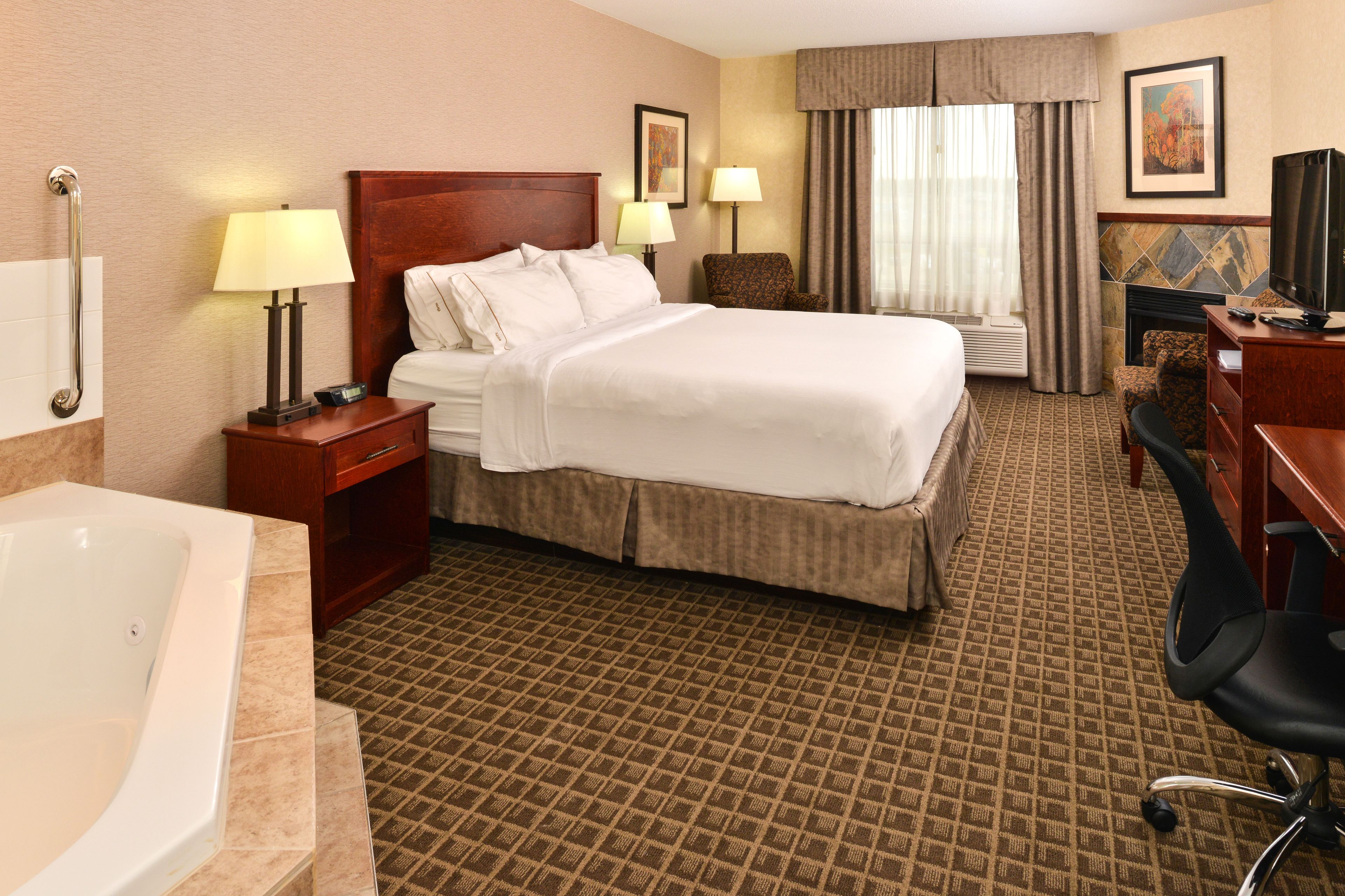Une chambre d’hôtel avec un grand lit, un bureau avec une chaise, une télévision, une cheminée et une salle de bain avec une baignoire.