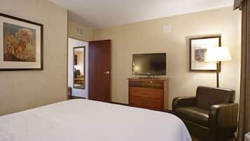 A hotel room with a large bed, a television on a wooden cabinet, a leather armchair, and a lamp.