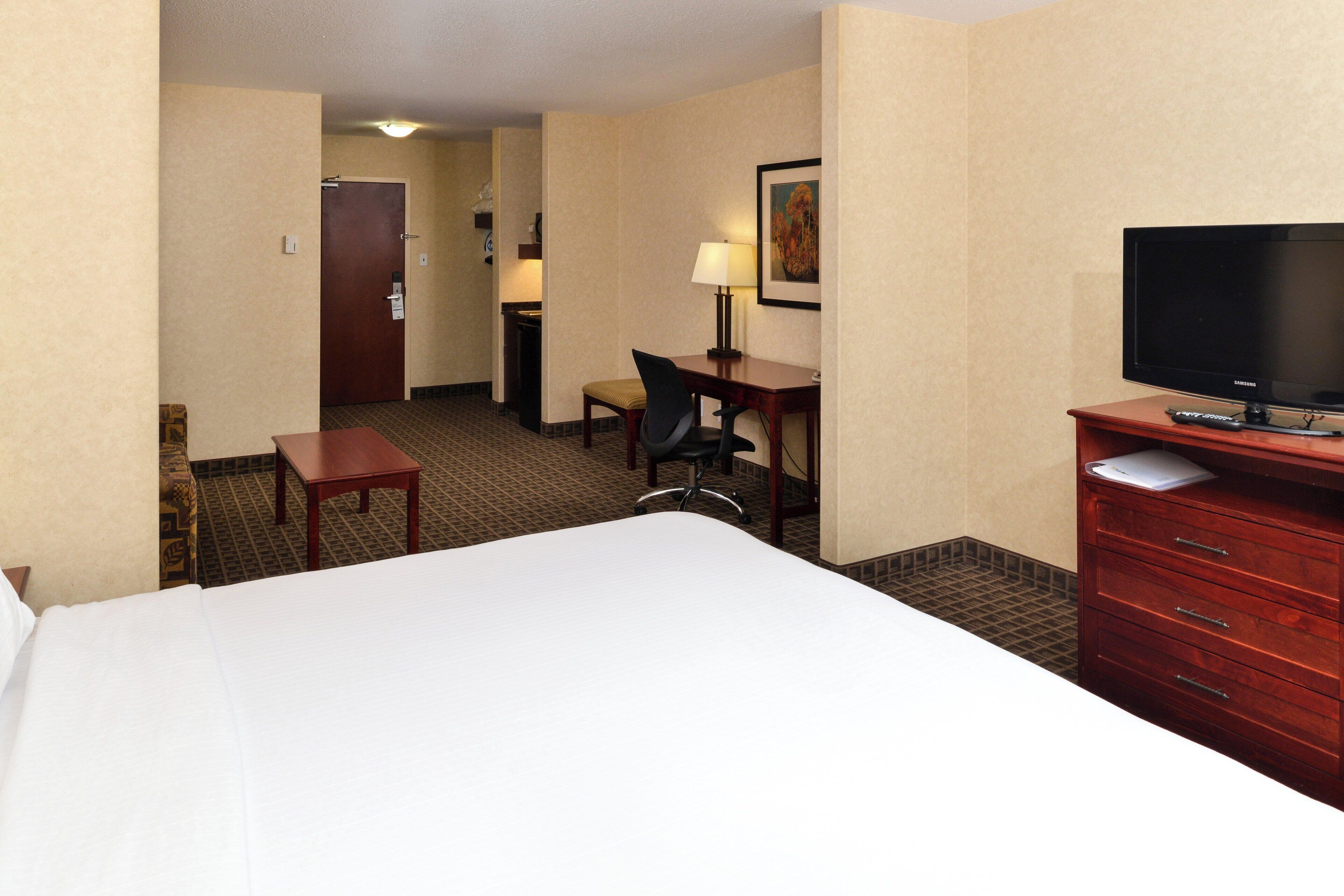 A hotel room with a bed, a desk, a chair, a television, and a dresser.