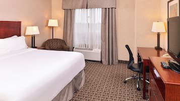 Habitación de hotel con una cama grande, un escritorio con televisor, una silla y una ventana con cortinas.