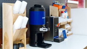 A coffee machine with a hot water dispenser, stacked cups, and a coffee pod holder. - Holiday Inn Express Hotel & Suites Edmonton North by IHG (Edmonton)