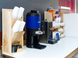 Une machine à café dotée d’un distributeur d’eau chaude, d’un compartiment pour les tasses et d’un support pour les capsules de café.