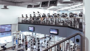 Academia com vários níveis, esteiras, máquinas de peso e um mezanino com equipamentos de ginástica.