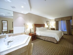 Une chambre d’hôtel avec un grand lit, une salle de bain séparée avec une baignoire et un petit coin salon.
