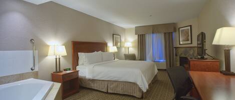 Une chambre d’hôtel avec un grand lit, deux tables de chevet avec des lampes, un bureau avec un ordinateur, une chaise, une salle de bain avec une baignoire et une fenêtre avec des rideaux.