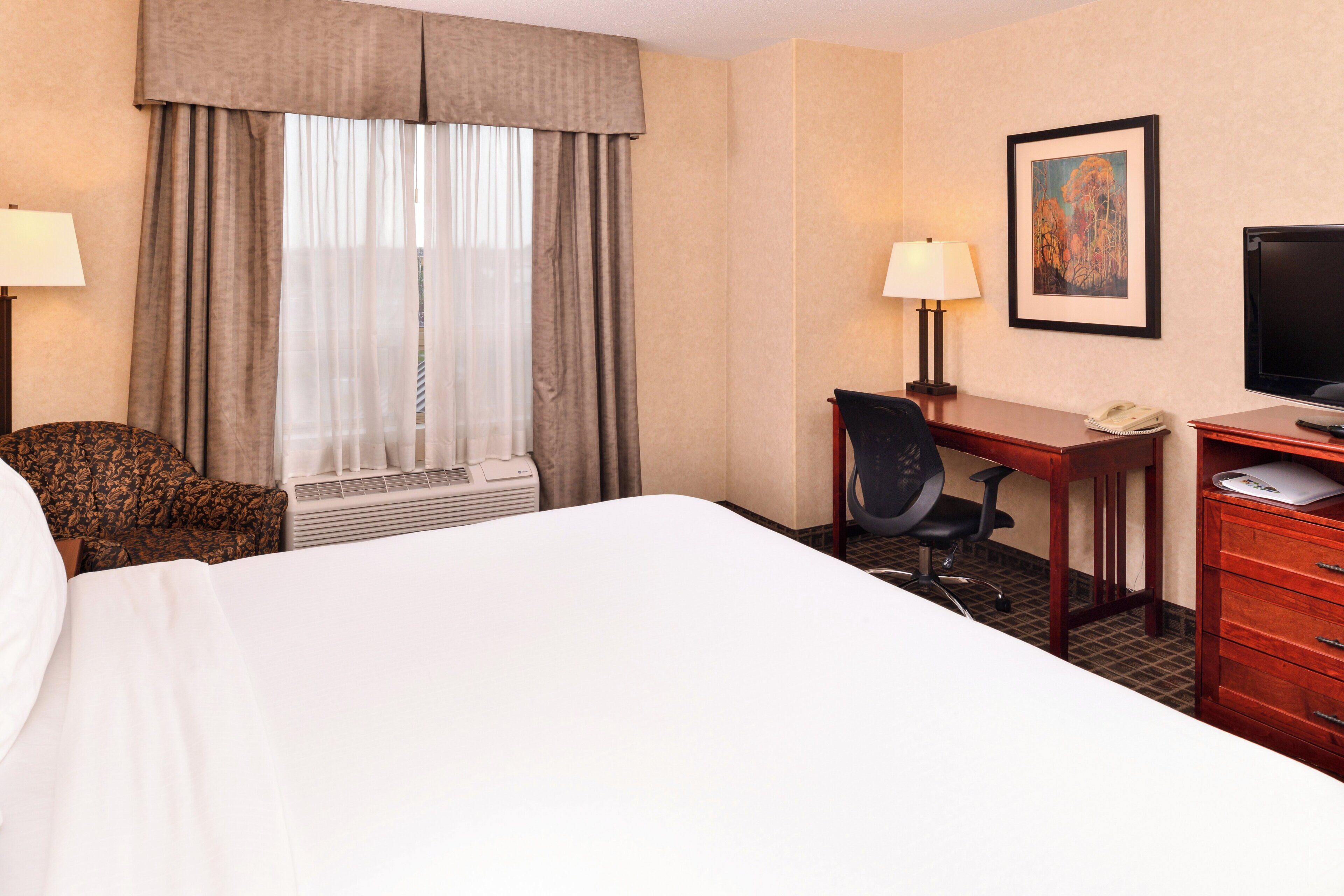 Une chambre d’hôtel avec un lit, un bureau, une chaise, une télévision et une fenêtre avec des rideaux.
