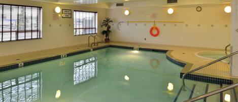An indoor swimming pool with clear water, safety signs, and a lifebuoy.