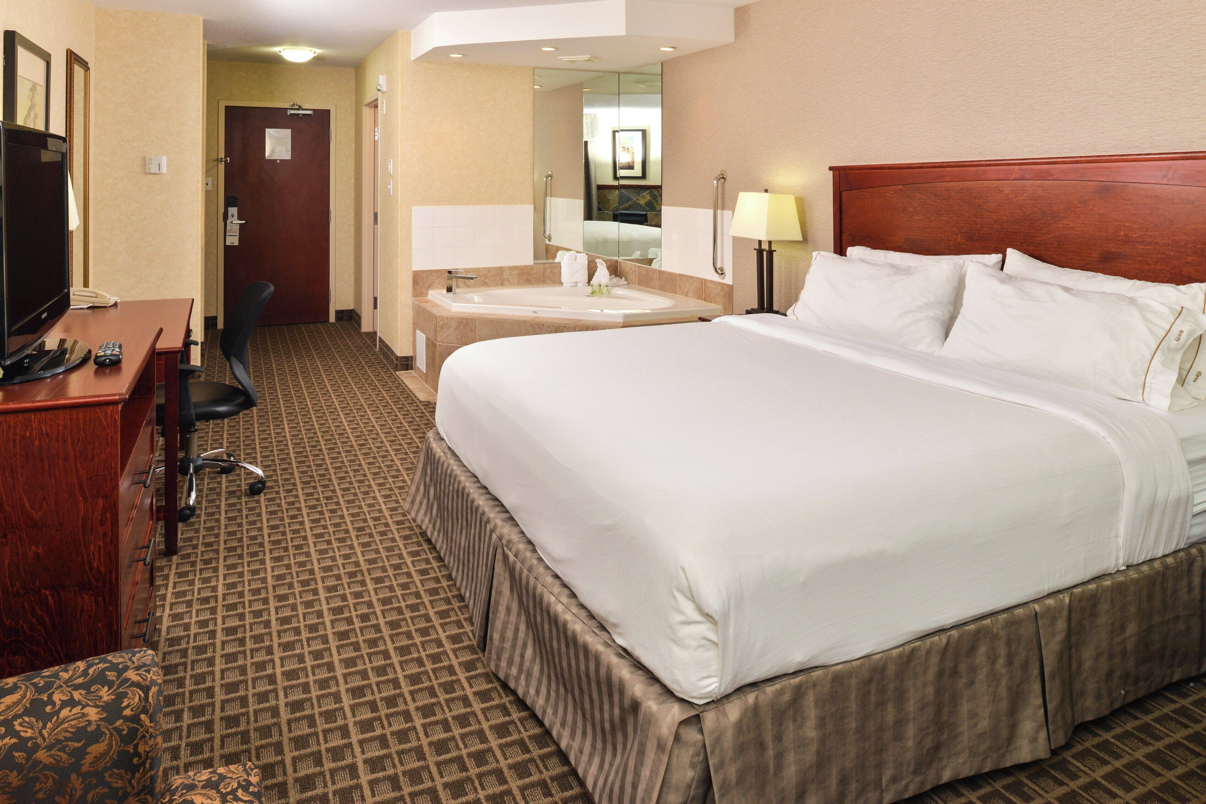 A hotel room with a large bed, a desk with a computer, a telephone, and a mirror.