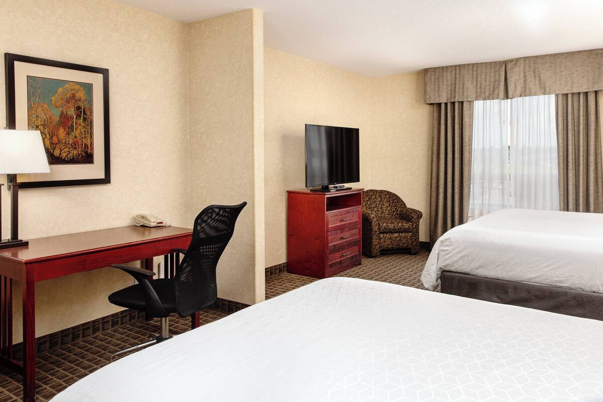 A hotel room with two beds, a desk with a chair, a television, and a framed picture on the wall.