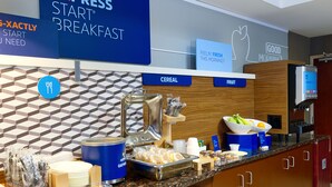 A breakfast buffet area with labeled sections for cereal and fruit, a coffee machine, and a sign promoting the breakfast service. - Holiday Inn Express Hotel & Suites Edmonton North by IHG (Edmonton)