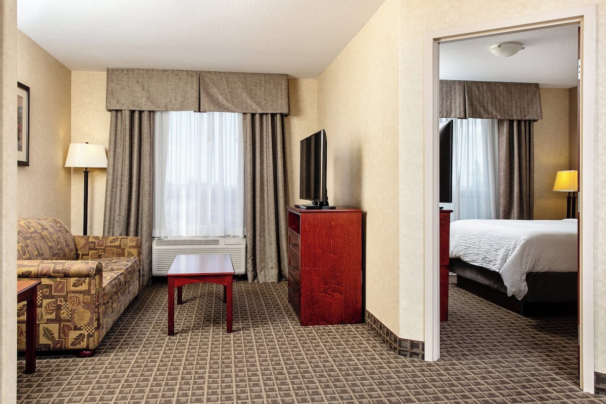 A hotel room with a sofa, a small table, a TV on a wooden stand, a bed, and a mirror.