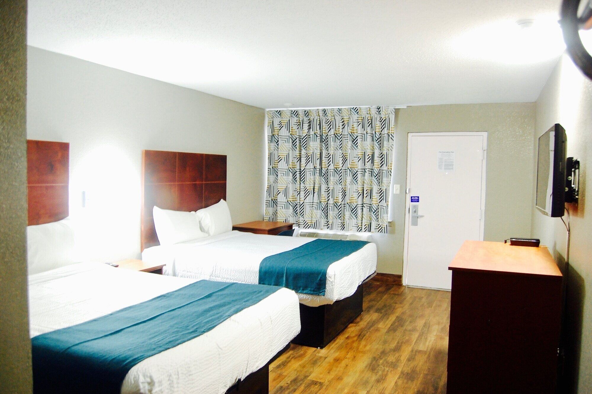 A hotel room with two beds, a desk, a TV, and a door.