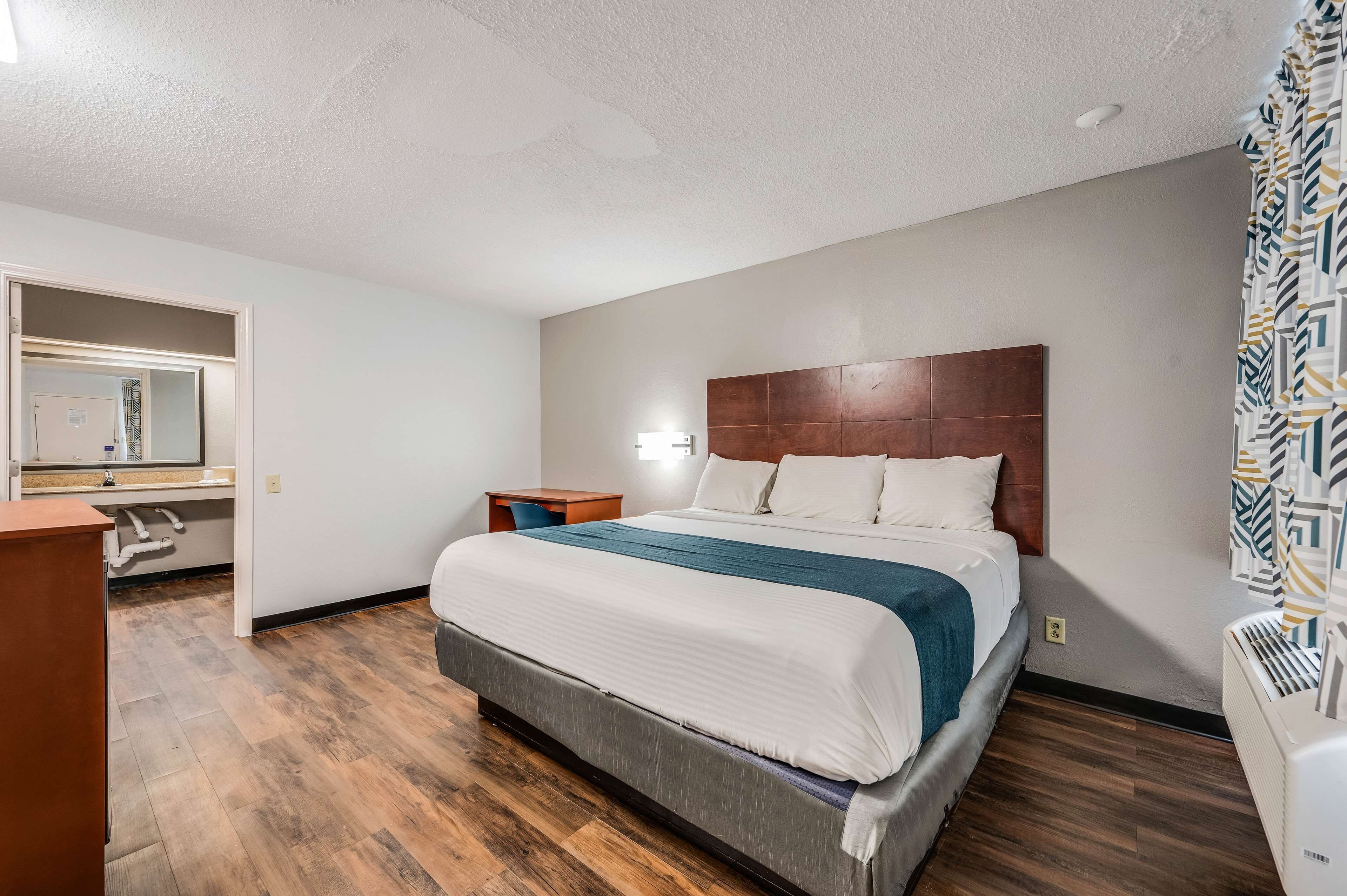 A hotel room with a large bed, a wooden headboard, a nightstand, a desk, and a mirror.
