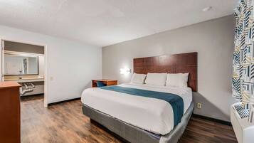 A hotel room with a large bed, a wooden headboard, a nightstand, a desk, and a mirror.