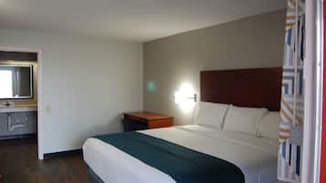 A hotel room with a bed, a nightstand, a mirror, and a bathroom with a sink and toilet.