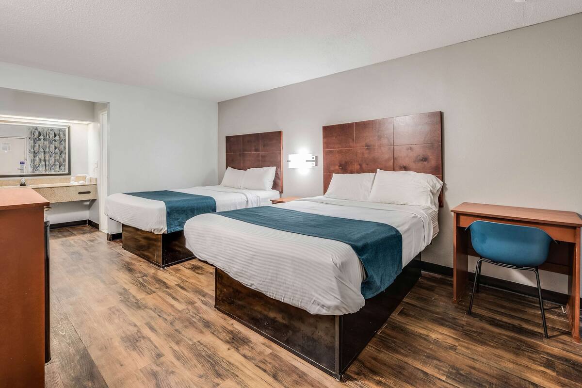 A hotel room with two beds, a desk, and a chair.