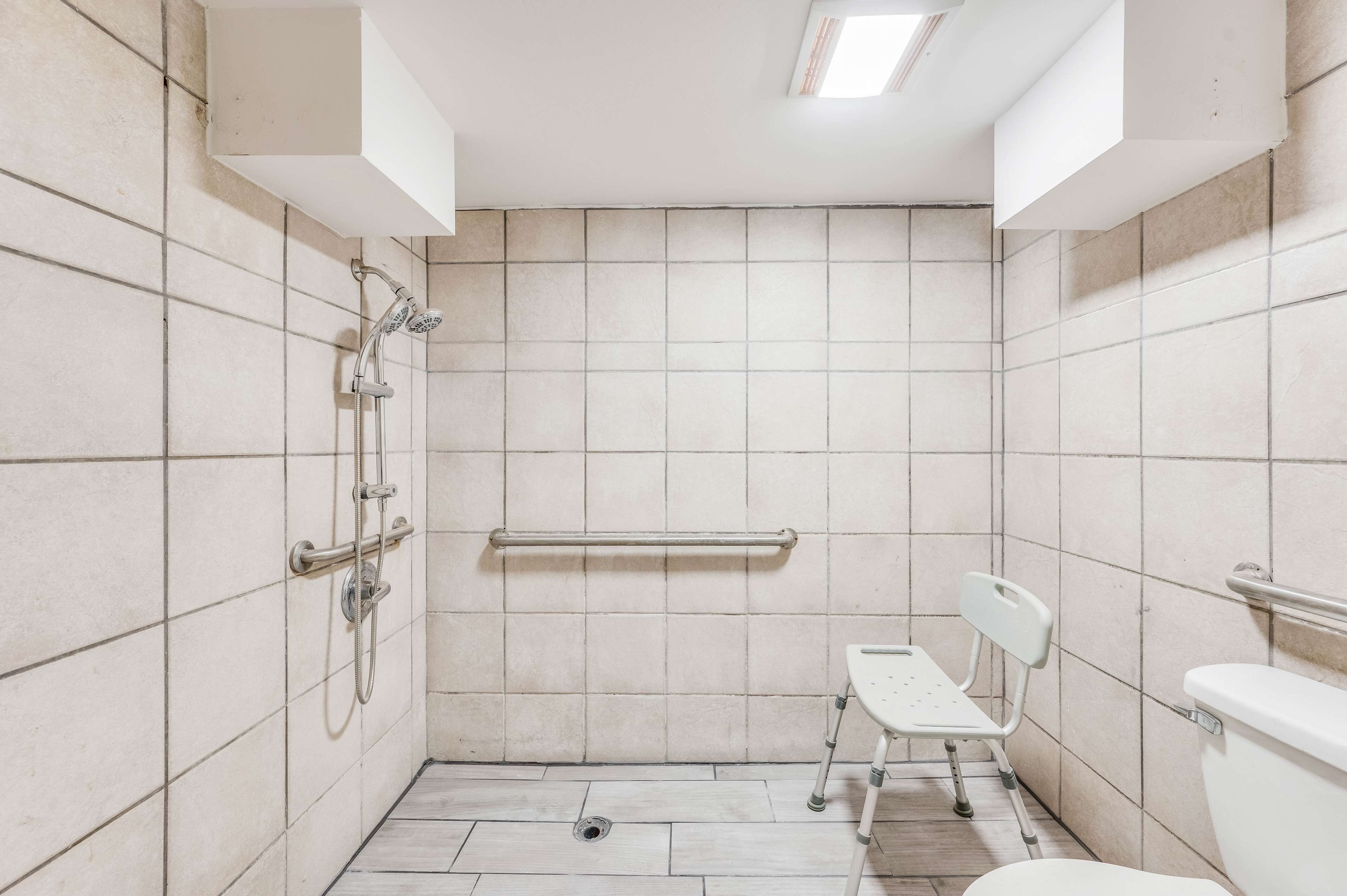 A small, tiled bathroom with a shower, a toilet, and a wheelchair-accessible bench.