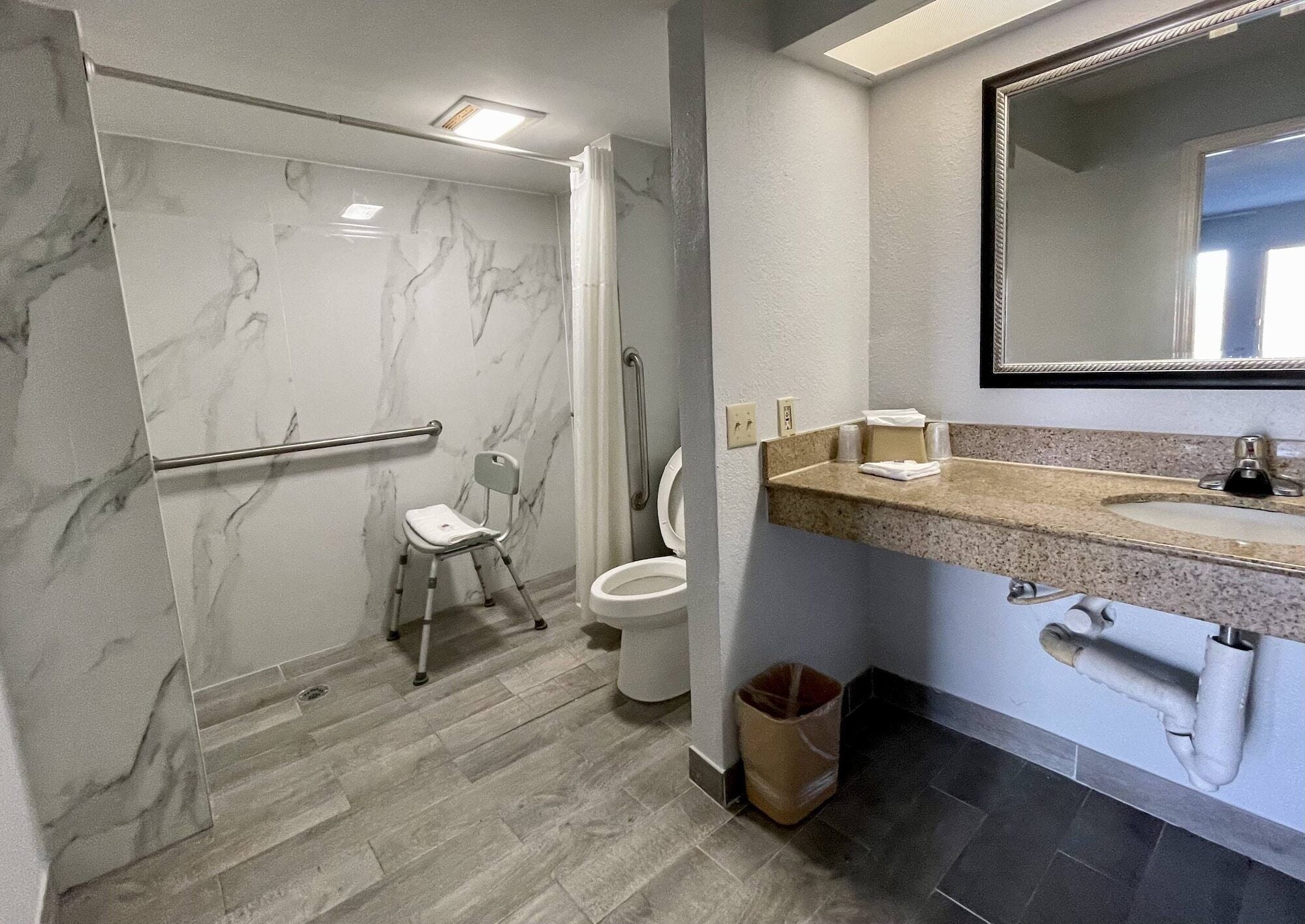 Une salle de bain avec une douche en marbre, des toilettes, un lavabo avec un miroir et une poubelle.