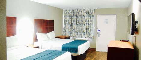 A hotel room with two beds, a wooden floor, a desk, a television, and a patterned curtain.