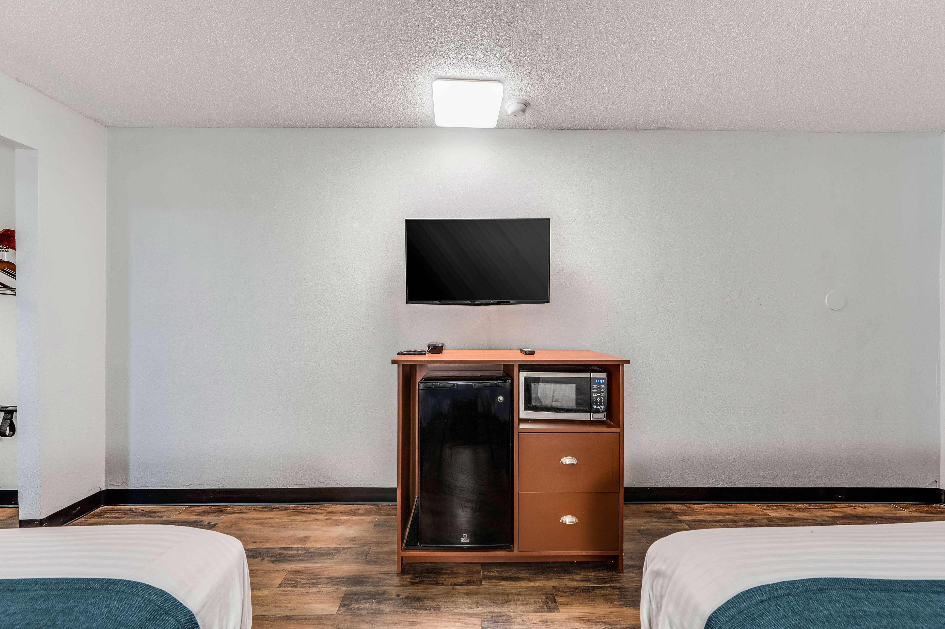 Une chambre d’hôtel avec deux lits, un téléviseur à écran plat fixé au mur, un minibar et un luminaire au plafond.