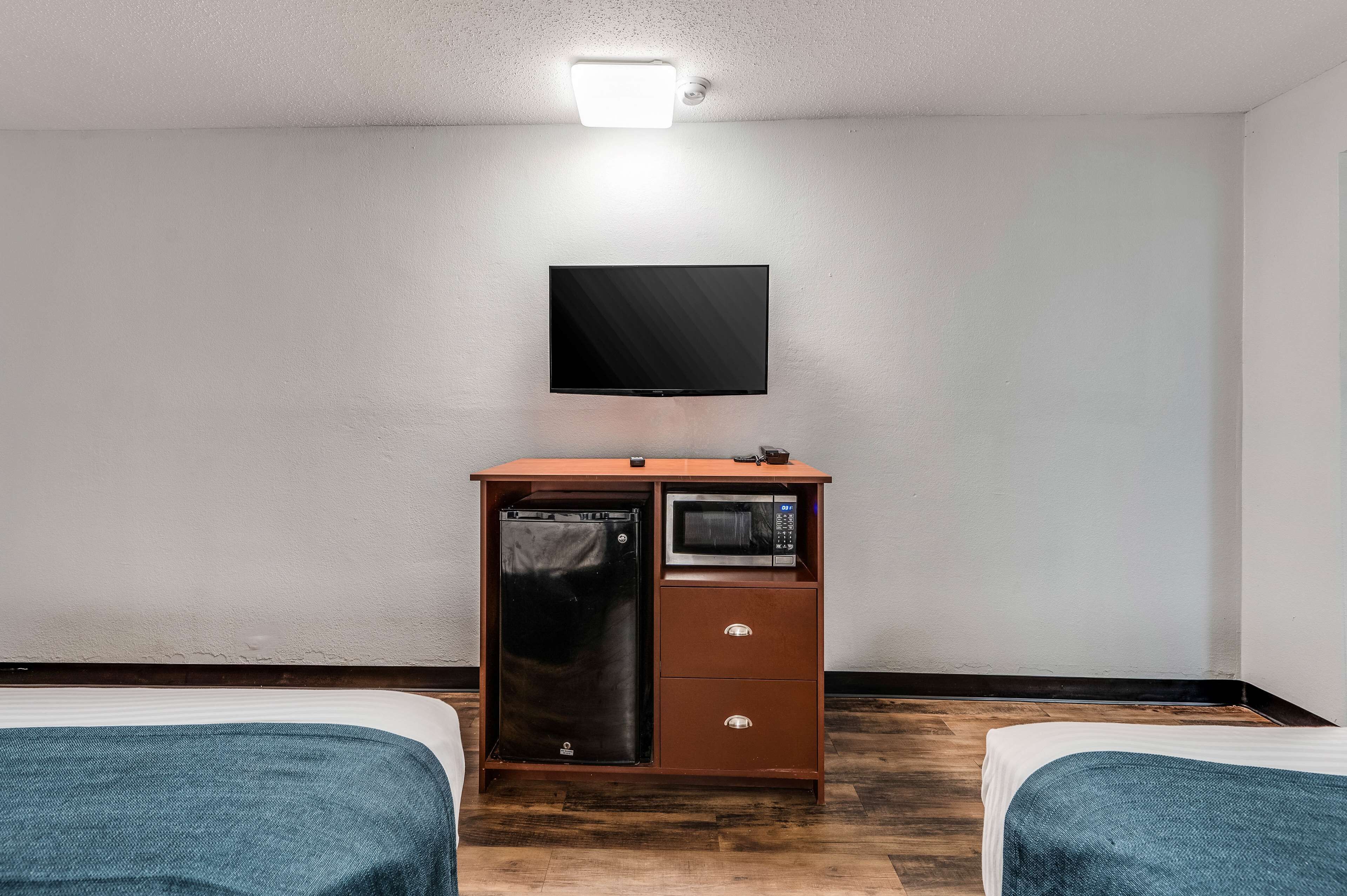 A hotel room with a bed, a TV mounted on the wall, a small refrigerator, and a microwave.