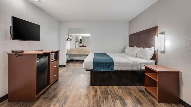 Ein Hotelzimmer mit Bett, Schreibtisch, Flachbildfernseher, Mikrowelle, Spüle und Spiegel.