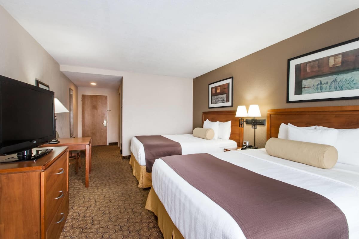 A hotel room with two beds, a TV, a desk, and a lamp.