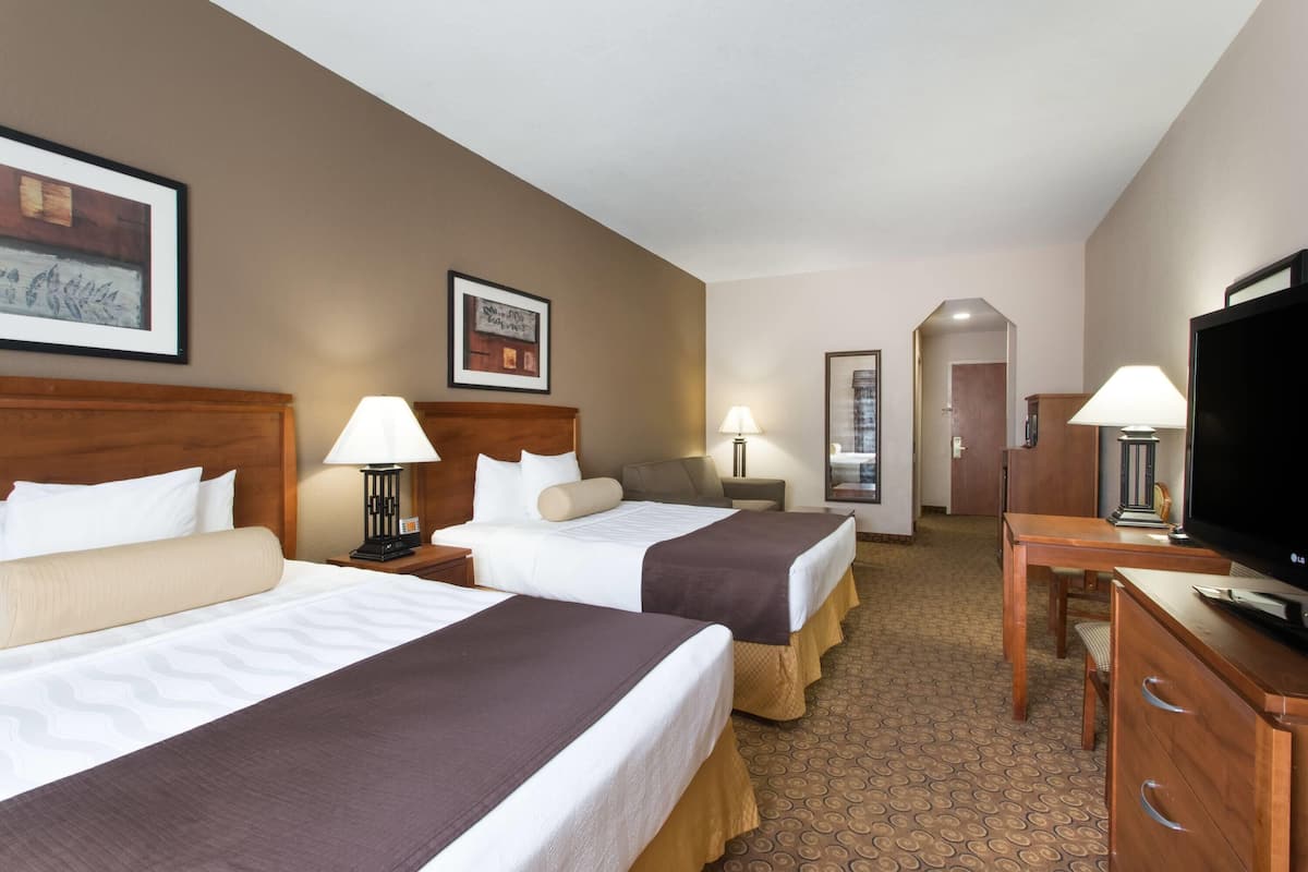 A hotel room with two beds, a TV, a desk, and a lamp.