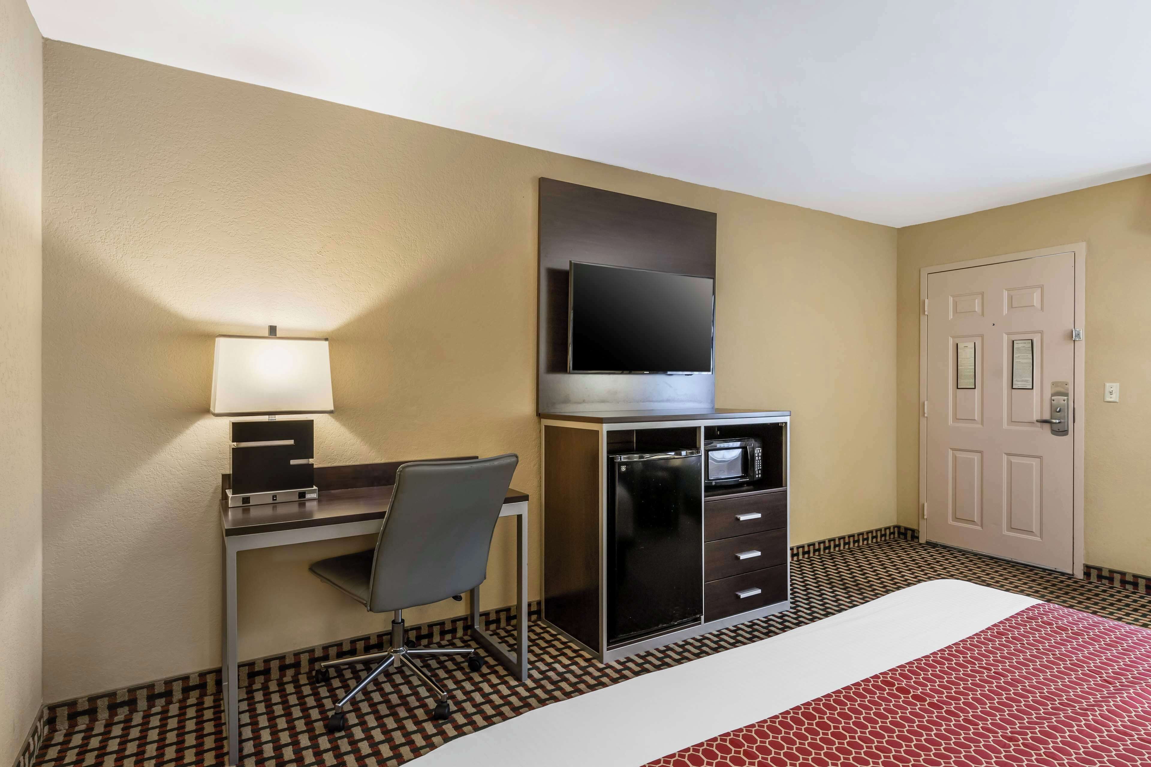 A hotel room with a bed, a desk with a chair, a television, a microwave, and a wardrobe.