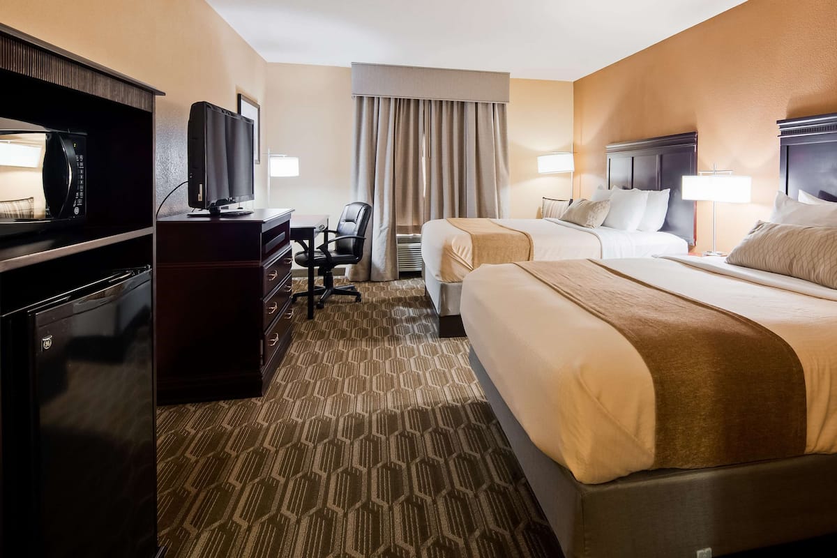 A hotel room with two beds, a desk with a television, a chair, and a lamp.