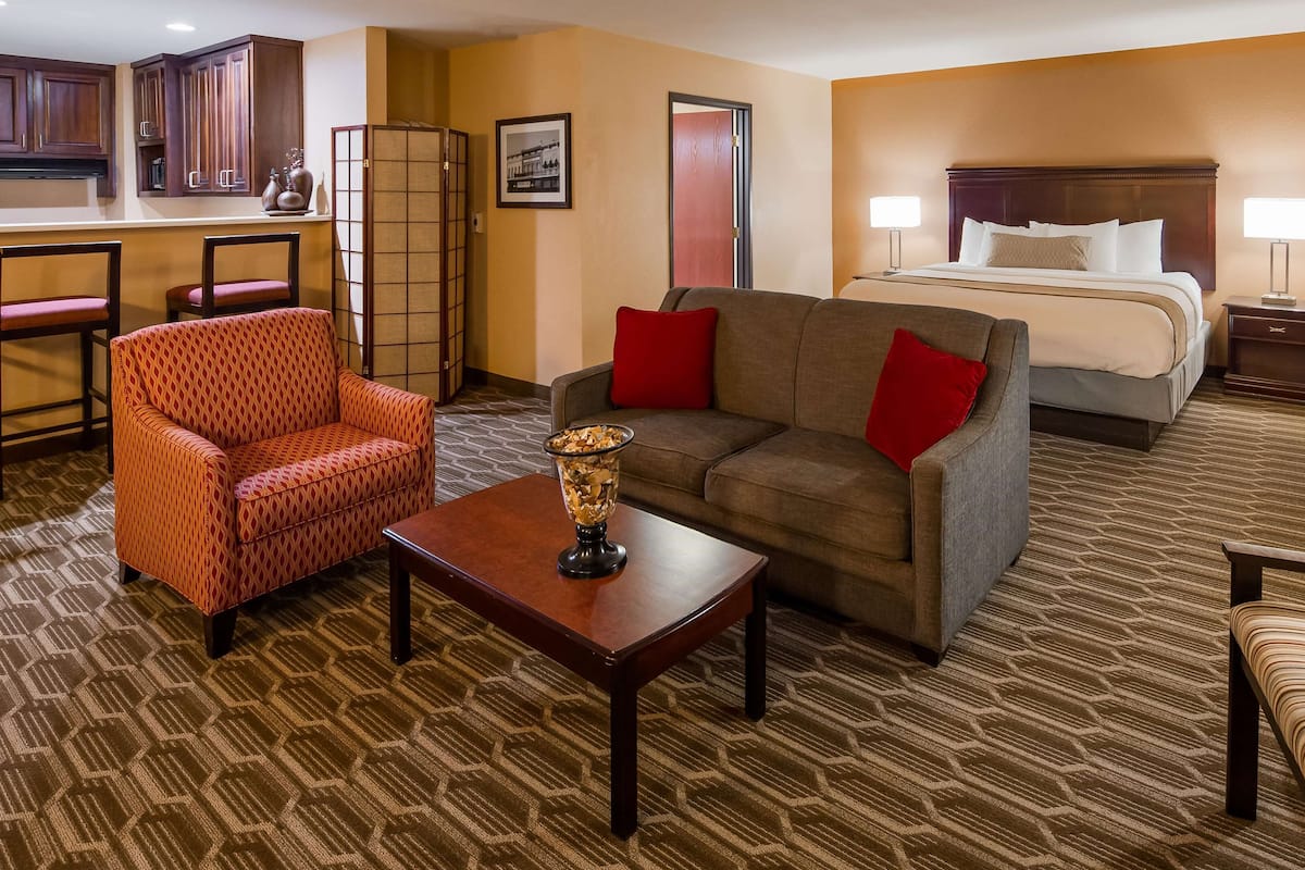 A hotel room with a sofa, armchair, dining table, and a bed with a nightstand.