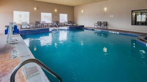 Una piscina interior con agua cristalina, un trampolín y sillones de descanso.