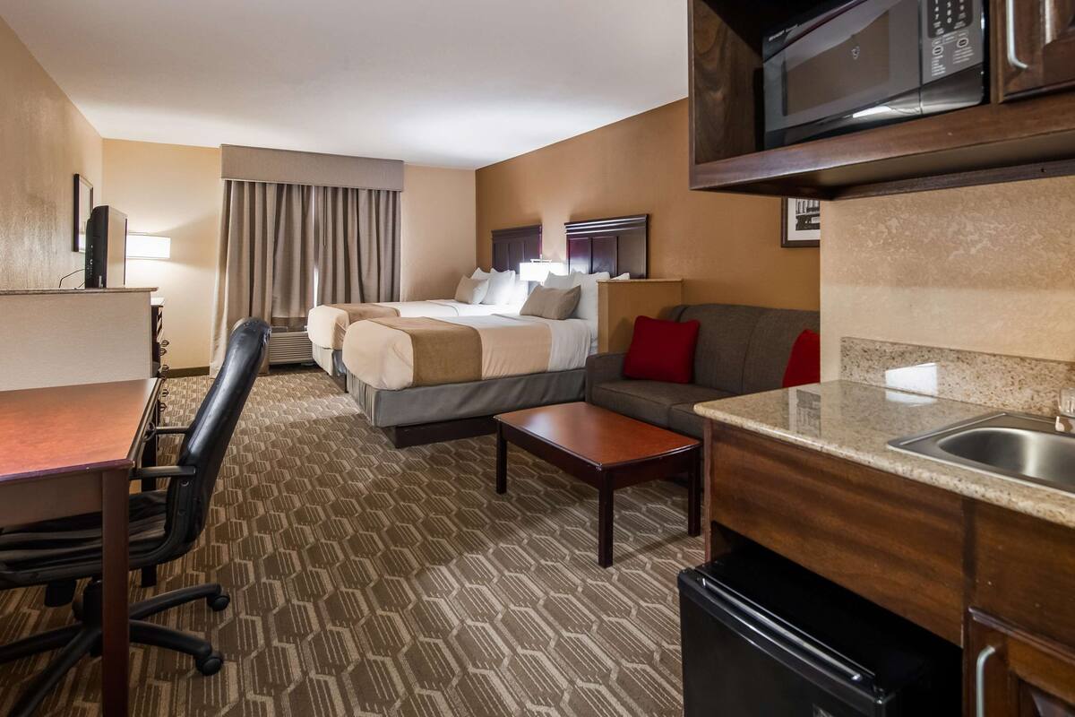 A hotel room with a bed, a sofa, a desk with a chair, a microwave, a sink, and a television.