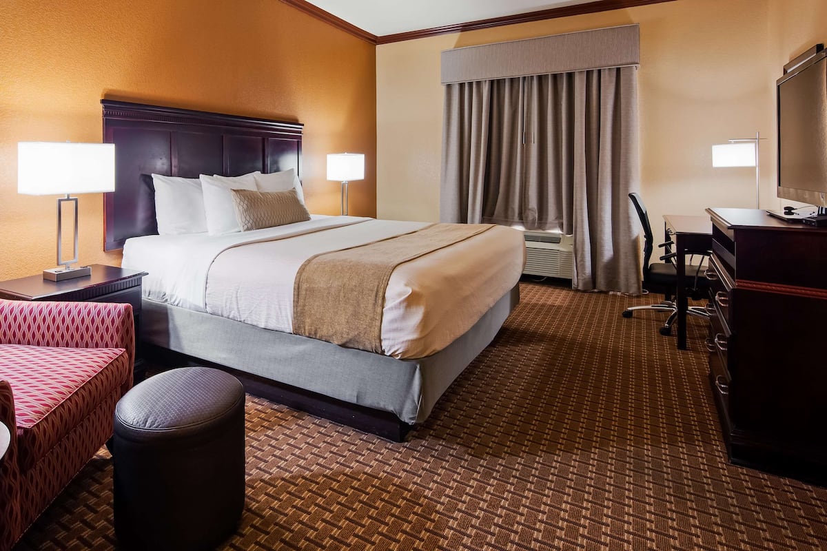 A hotel room with a large bed, a desk, a chair, and a small table.