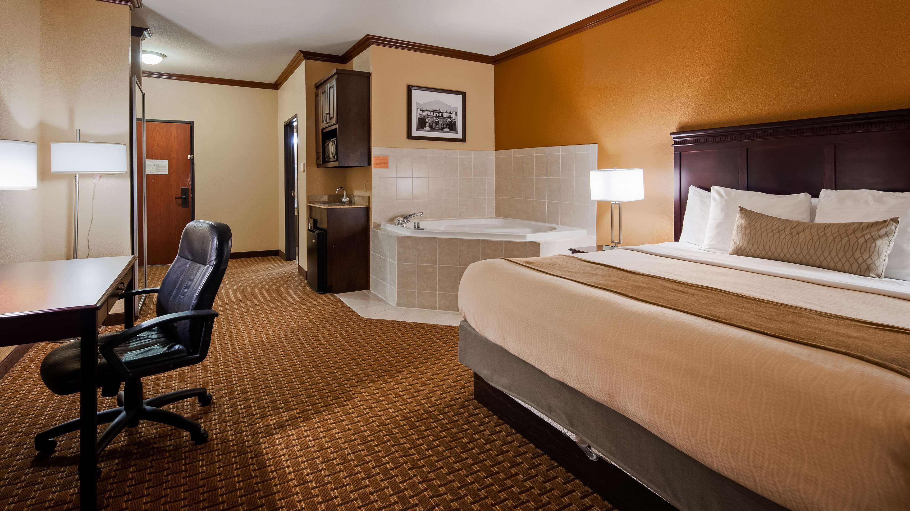 Een hotelkamer met een bed, een bureau, een stoel, een badkamer met bad en een foto aan de muur.