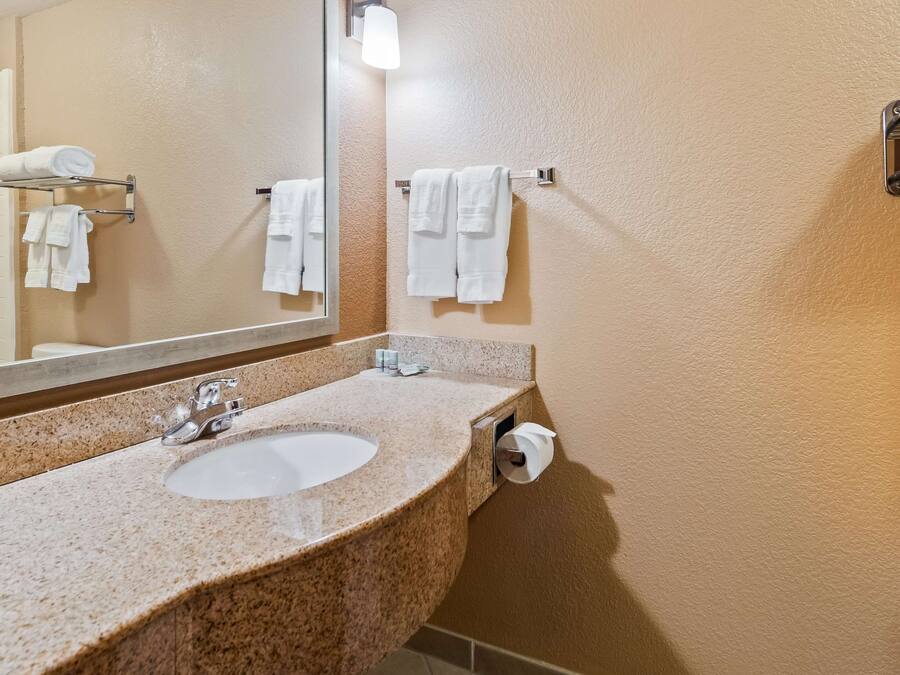 Une salle de bain avec un lavabo doté d’un plan de travail en granit, un miroir, un porte-serviettes et des toilettes.