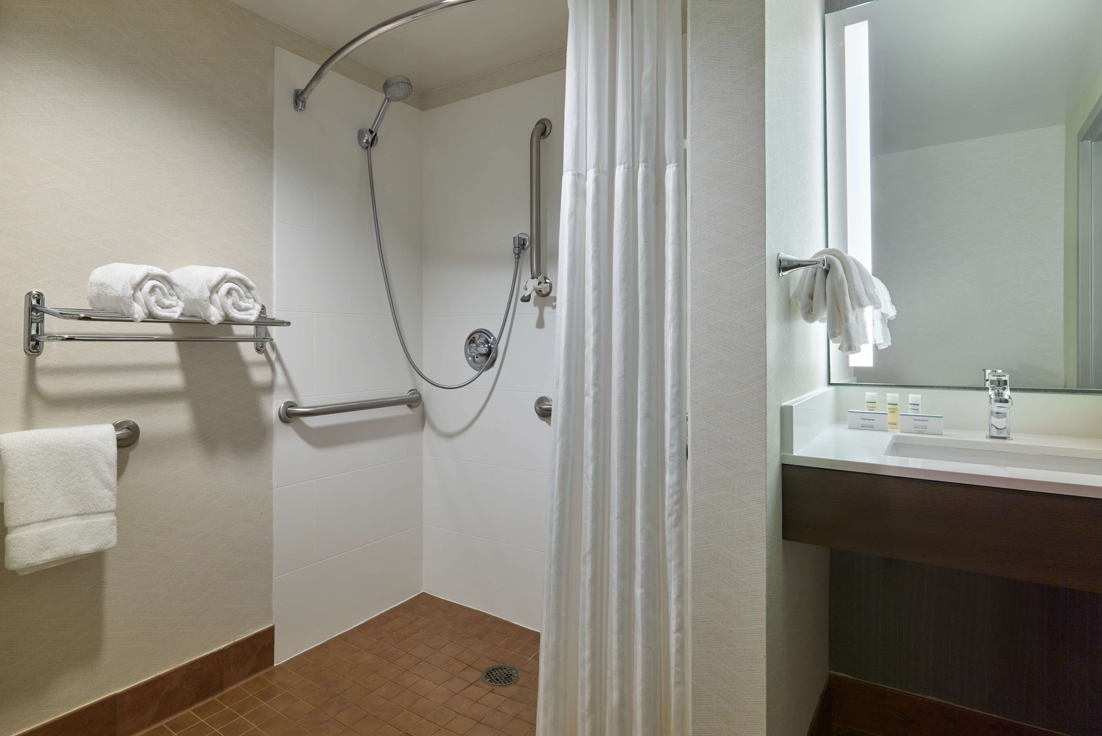 A bathroom with a shower, a towel rack, a sink, and a mirror.