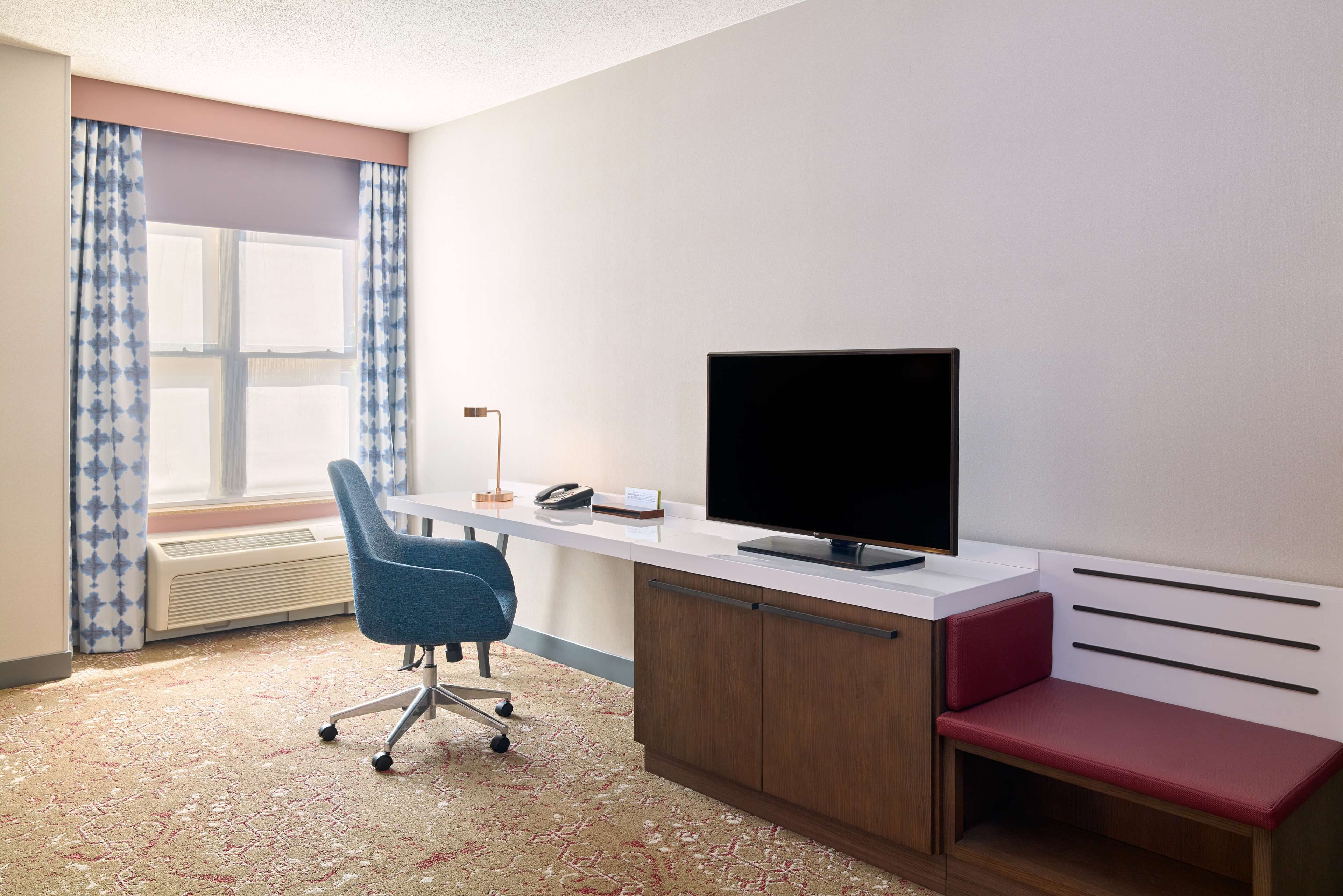 A room with a desk, chair, television, and a window with curtains.