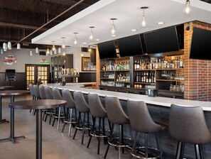 A bar area with a long counter, multiple stools, and a variety of liquor bottles and glasses. - Hilton Garden Inn Bloomington (Bloomington)