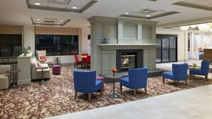 A lobby with a fireplace, seating area, and a view of the outside. - Hilton Garden Inn Bloomington (Bloomington)