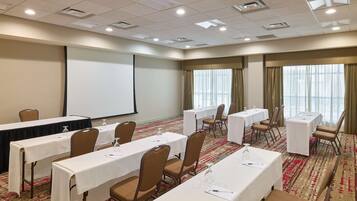 A conference room with tables, chairs, a projector screen, and a carpeted floor.