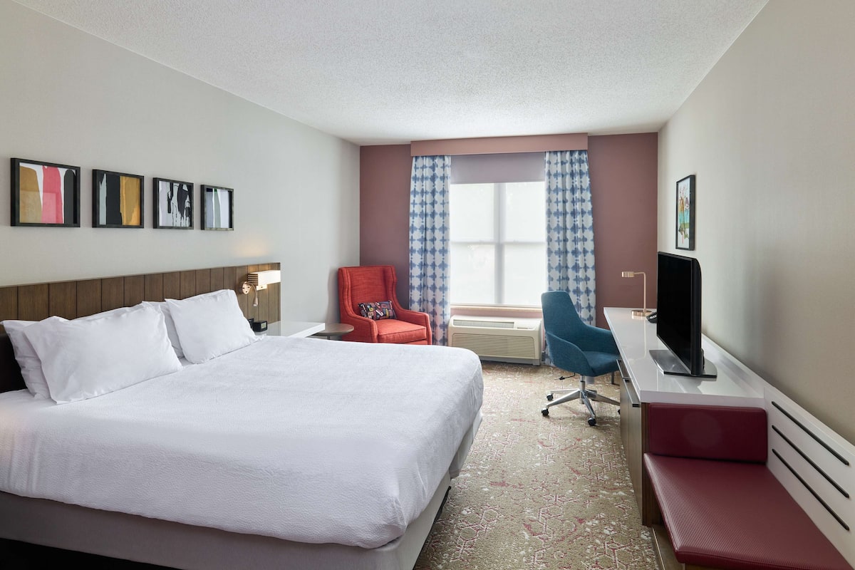 A hotel room with a large bed, a desk with a TV, a chair, and a window with curtains.