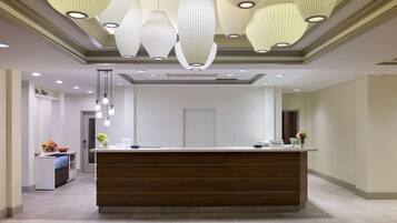 Un espace d’accueil d’hôtel avec un comptoir de réception en bois, des luminaires suspendus et un mur blanc à texture.