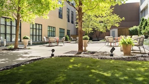 A courtyard with outdoor seating, trees, and a building with large windows. - Hilton Garden Inn Bloomington (Bloomington)