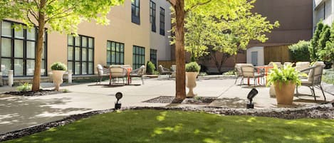 A courtyard with outdoor seating, trees, and a building with large windows.