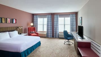 A hotel room with a bed, a desk, a chair, a TV, and a window with patterned curtains.