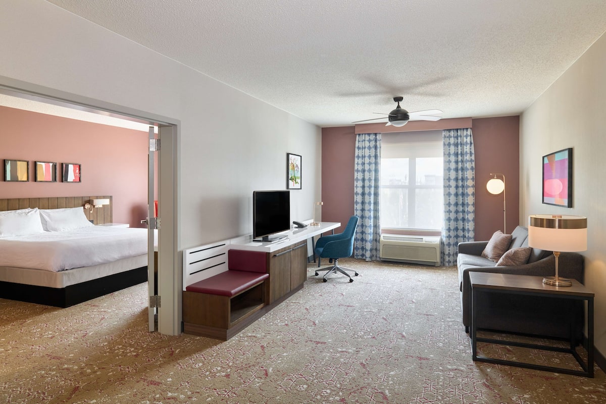 A hotel room with a bed, desk, chair, sofa, and a ceiling fan.