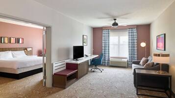 Quarto de hotel com cama, escrivaninha, cadeira, sofá e ventilador de teto.